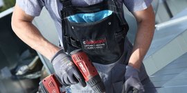 Der Arbeiter trägt eine schwarze Latzhose mit dem Logo 'CLIMAVENT' und arbeitet konzentriert mit einem Akkuschrauber.