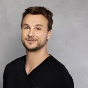 Der Mann hat kurzes, braunes Haar und einen gepflegten Bart, während er freundlich in die Kamera schaut.